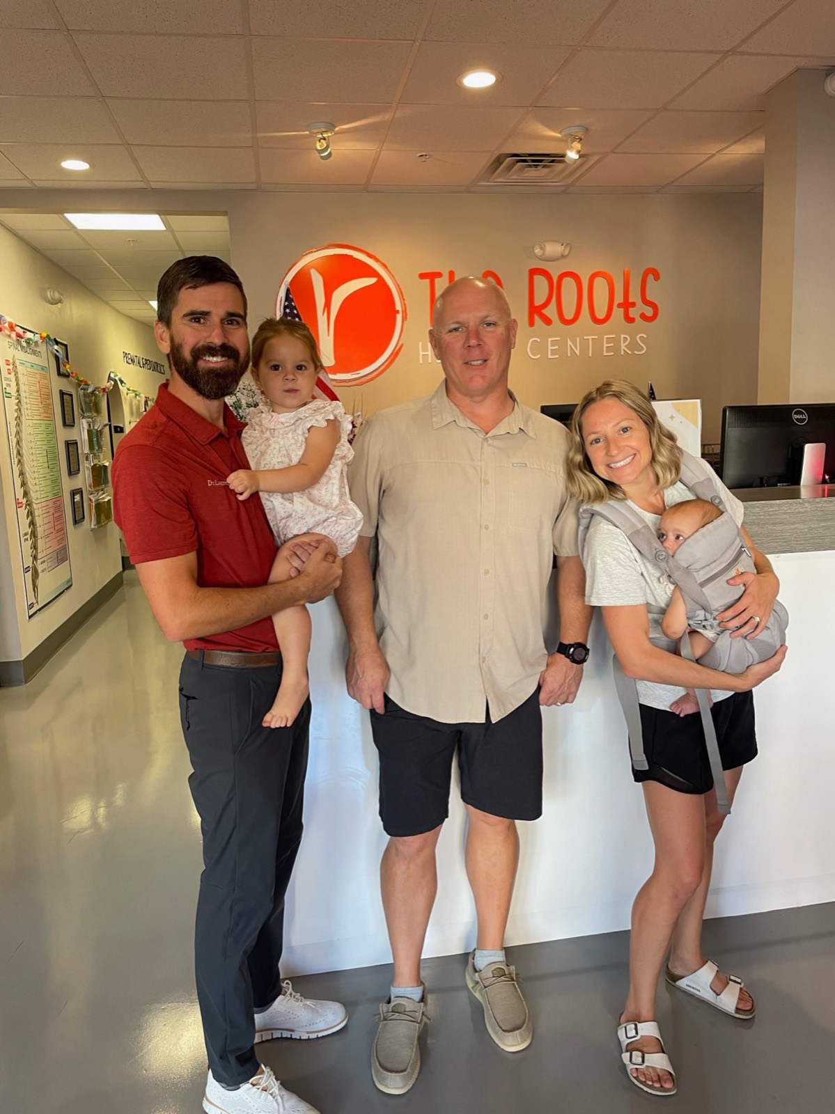 Families gather with their newborn at The Roots logo wall.
