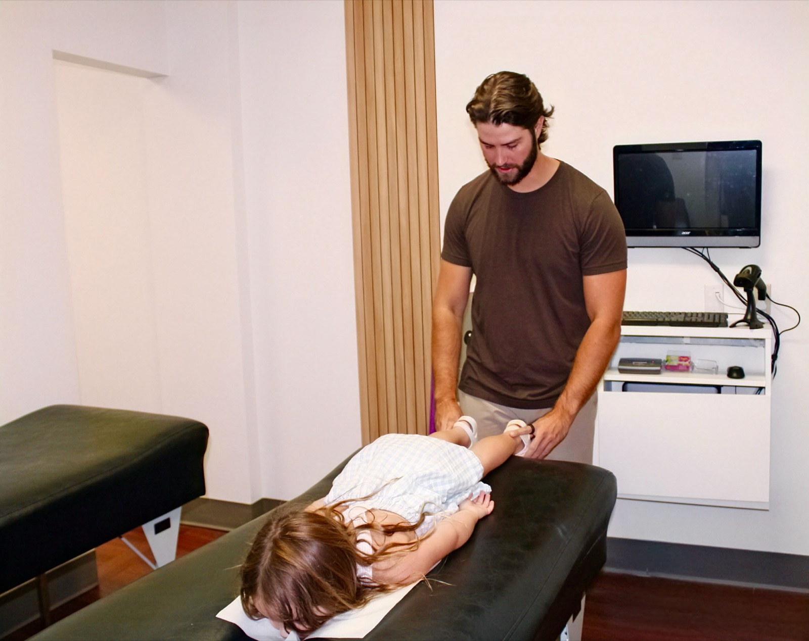 A smiling toddler lies on a pediatric adjustment table with Dr. Fox.