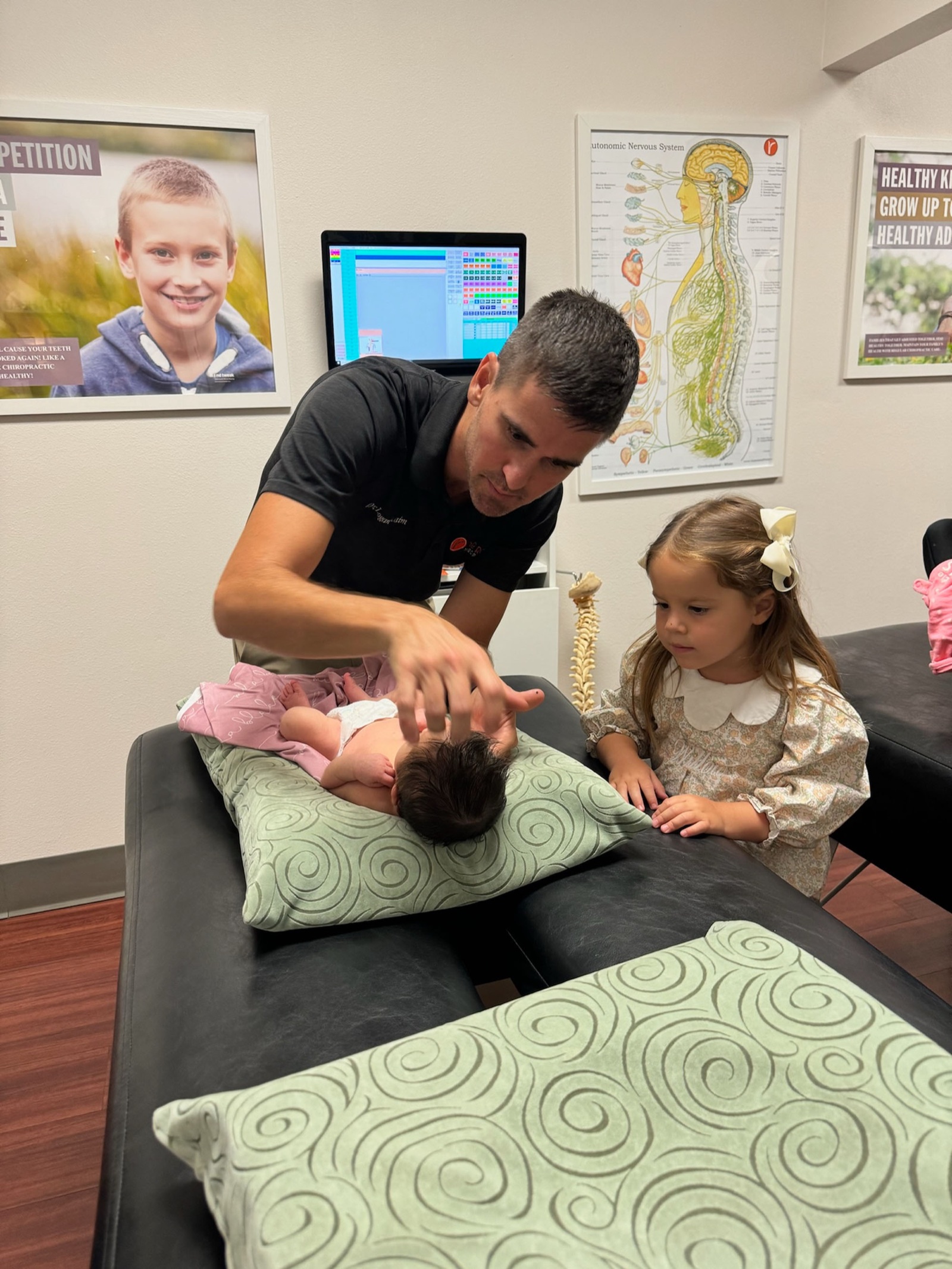 Dr. Logan adjusts a baby as her older sister looks on.