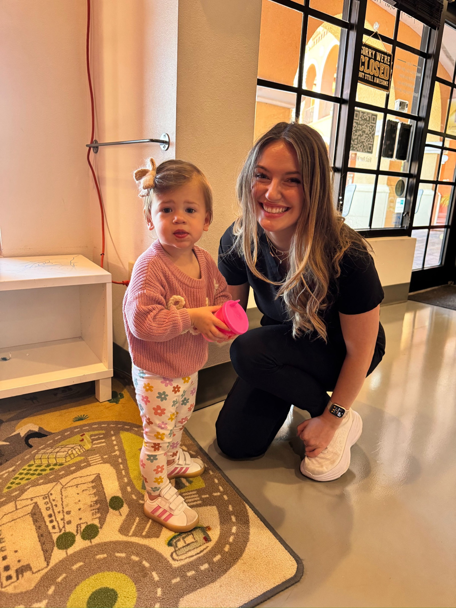 Carly kneels with a young patient by the signature Roots arch.